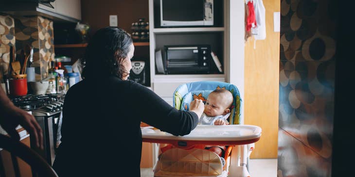 Nanny feeding a baby in the kitchen.