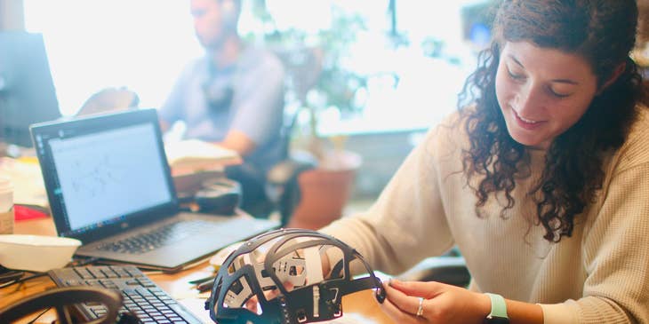 Female NDT technician examining a helmet structure on her workstation with an open laptop.
