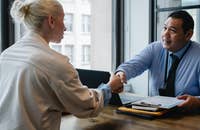 Una empleadora estrechando la mano de un empelado que acaba de recibir un correo electrónico y carta de bienvenida para nuevos empleados.