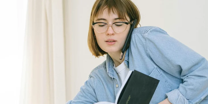 An operations associate talking on the phone while checking a schedule book.