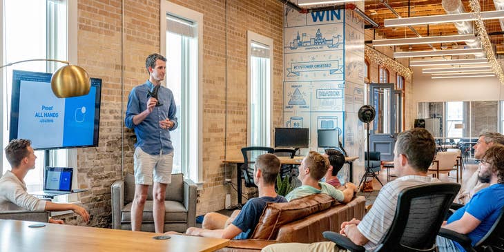 Operations manager of a startup company conducting a briefing regarding updates on the company's policies while the rest of the team looks on