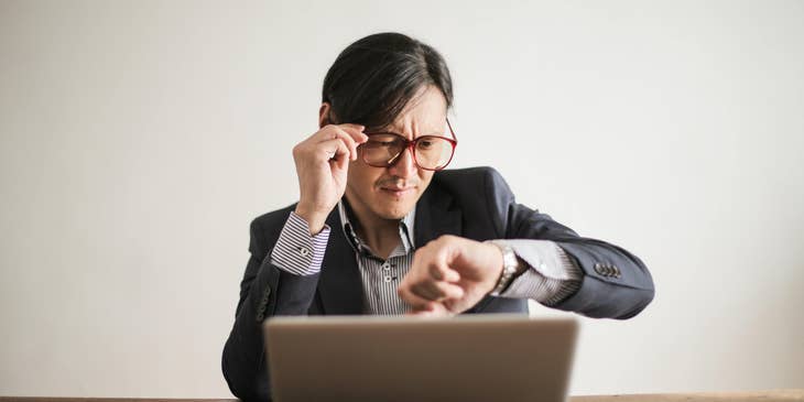 Un hombre trabaja con su laptop y revisa su reloj de pulsera.