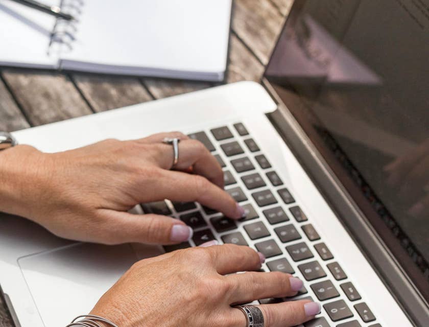 A payroll director typing on a laptop next to an open notebook.