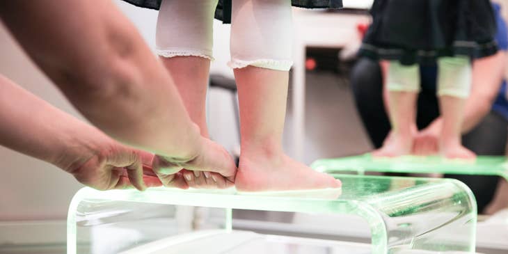 Pediatric physical therapist helps a young patient to balance feet during the therapy session.