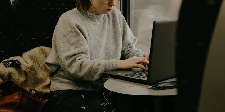 Female Pega developer wearing eyeglasses and earphones while typing on her laptop.