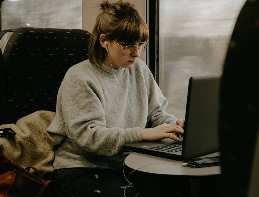 Female Pega developer wearing eyeglasses and earphones while typing on her laptop.