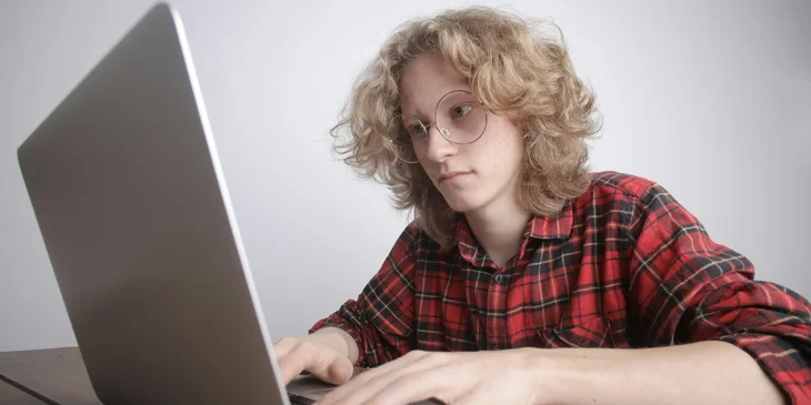 A Pega developer wearing glasses and earphones while typing on a laptop.