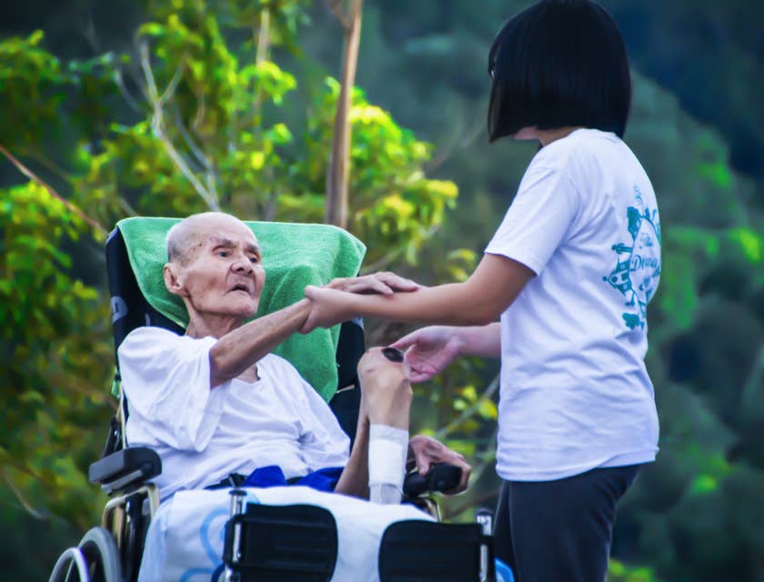 Personal care assistant holds the hand of elder patient as mobility support.