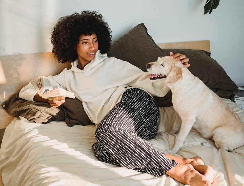 Pet sitter lounging on bed and holding a book while petting a white dog