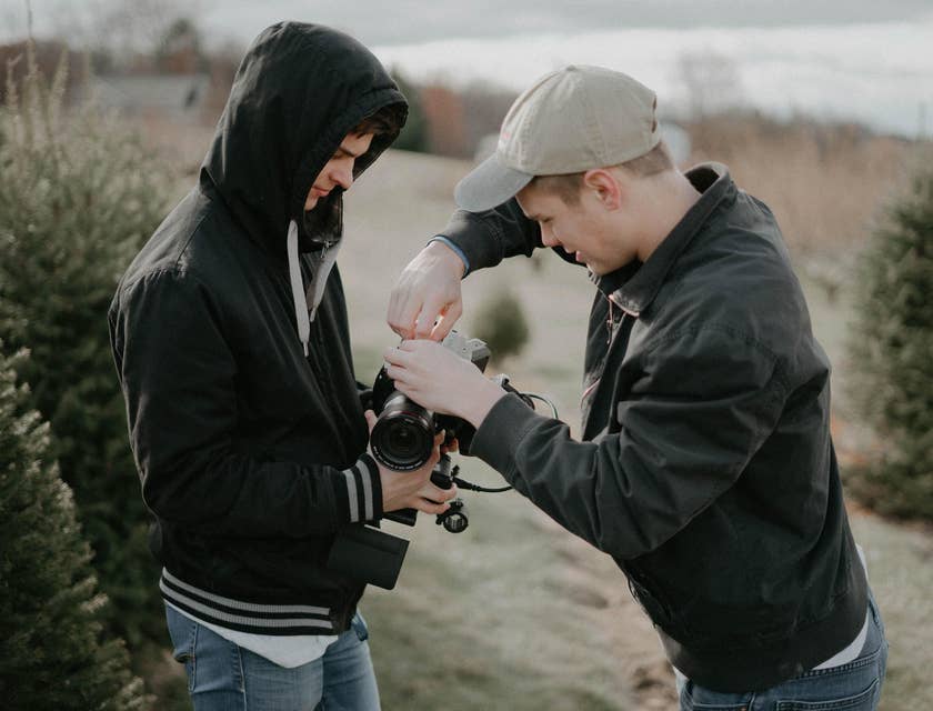 A photographer fixing his DSLR while his photographer assistant is holding it