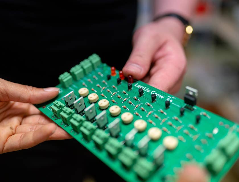 Physical design engineer holding a circuit board and showing to his colleague for further optimization.