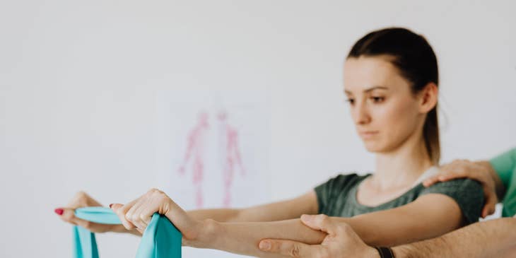 Physical therapist assistant guides the patient in muscle stretching using an elastic band.