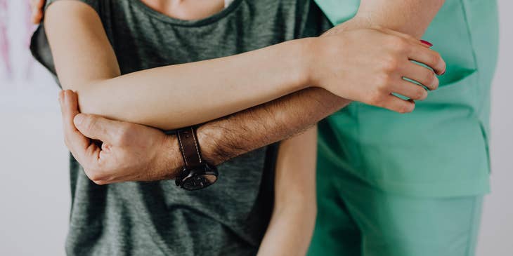 Physical therapy aide carefully supports patients shoulder as she sits down.