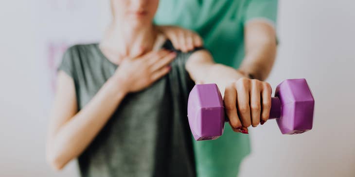 Physical therapy technician assists a patient in a light exercise using a dumbbell.