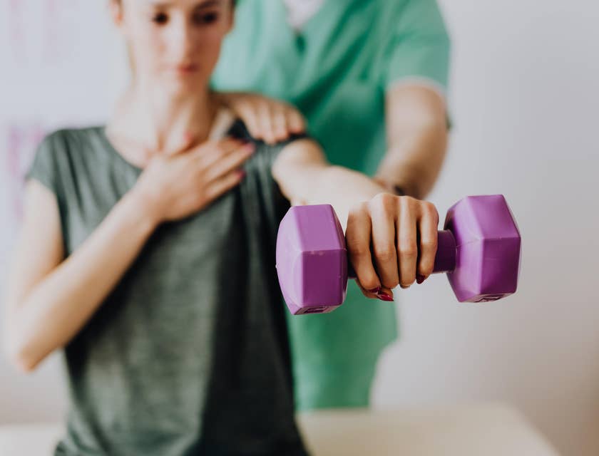 Physical therapy technician assists a patient in a light exercise using a dumbbell.
