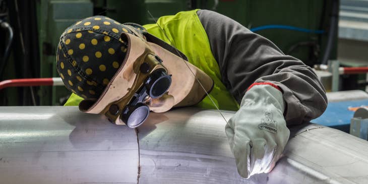 Welder in full protective gear welding a pipe.