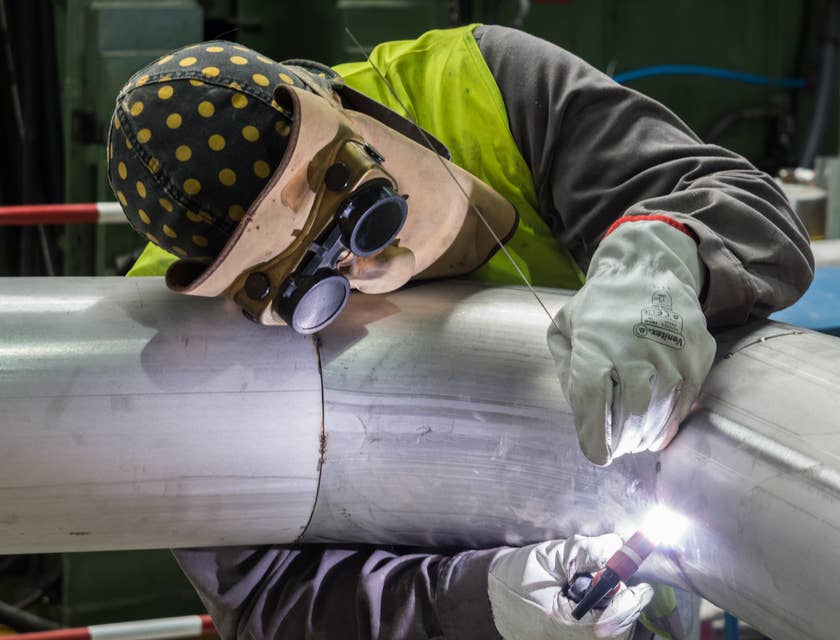 Welder in full protective gear welding a pipe.