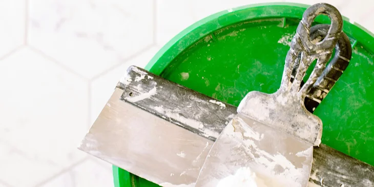 A wall plaster on metal scraper and green lid.