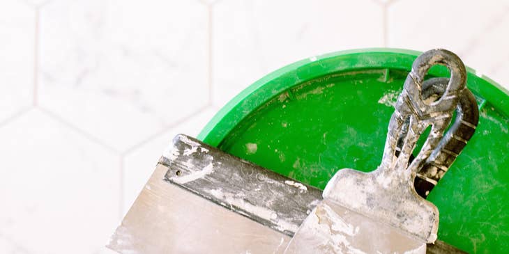 Wall plaster on metal scraper and green lid.