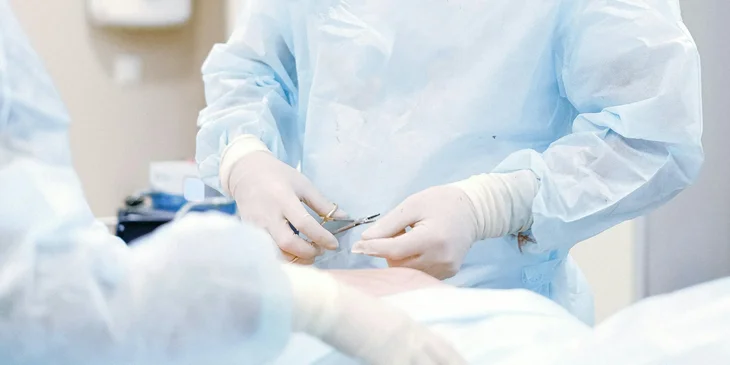 A plastic surgeon cutting a surgical thread as he finishes an operation.