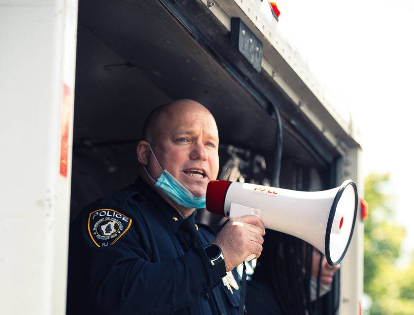A police sergeant on duty talking through a megaphone and assisting his subordinates during a protest.