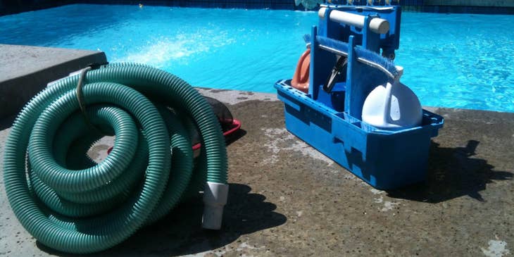 Cleaning equipment of a pool service technician beside a swimming pool.