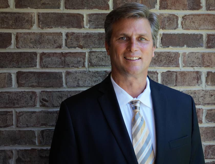 Portrait of a portfolio manager wearing a business suit and smiling against a brick wall.