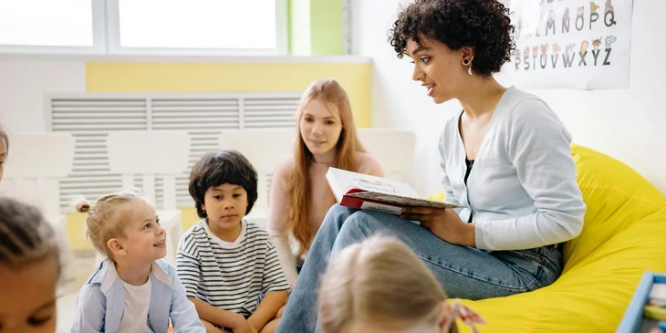 A preschool teacher reading an interactive storybook to toddlers.