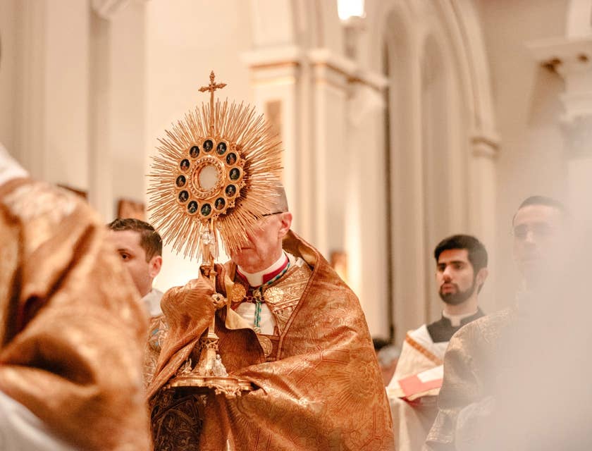 a priest holding the golden cross during the opening of the Mass