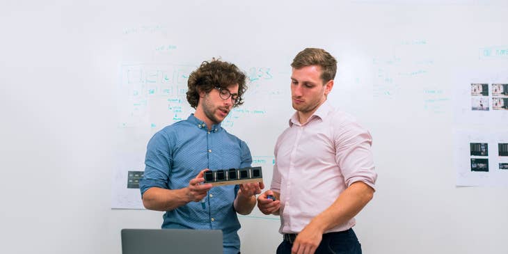 two product development engineers discussing the product at hand while standing by the whiteboard