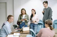 Un profesor revisando un trabajo de investigación en un portátil con un grupo de estudiantes universitarios.