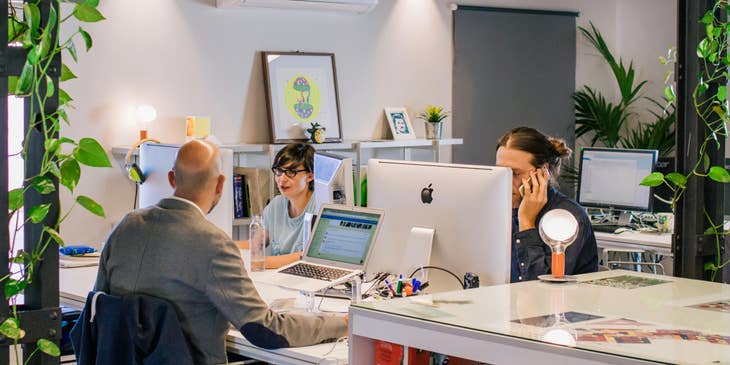 A team of programmer analysts discussing something while sitting at their respective workstations.