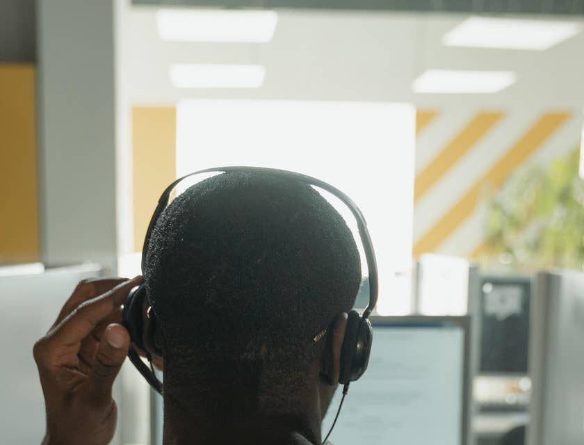 A progressive claims adjuster trainee in an office setting with a headset on his ears in front of a computer.