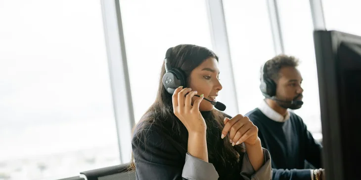 A progressive claims adjuster trainee in an office setting with headset on her ears in front of a computer.