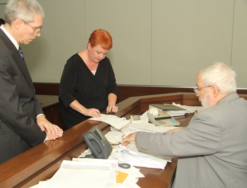 A Male Prosecutor with a female client in front of a judge in a courtroom signing documents.