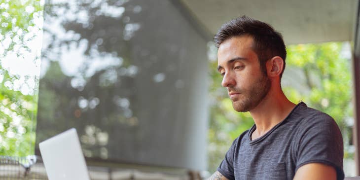 male Python developer looking at the screen of his laptop while sitting