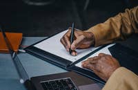 Una persona trabajando en su computadora portátil y tomando notas.