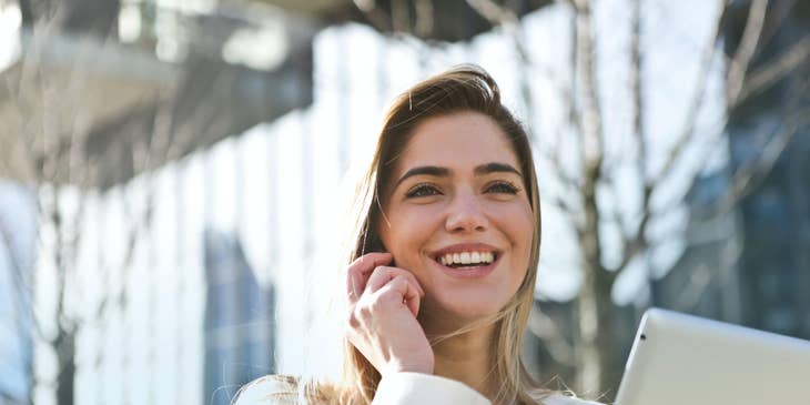 a smiling relationship manager speaking to her client through a mobile phone while holding her tablet on the other hand