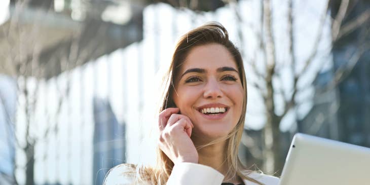 a smiling Relationship Manager speaking to her client through a mobile phone while holding her tablet on the other hand