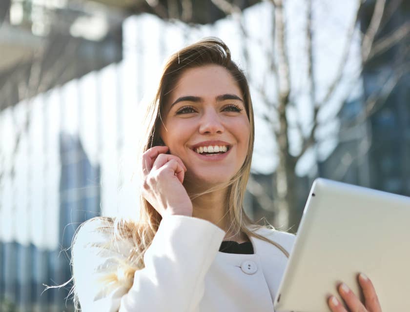 a smiling Relationship Manager speaking to her client through a mobile phone while holding her tablet on the other hand