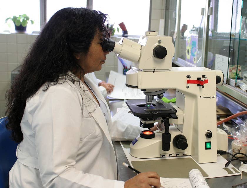 Research scientist looking down a microscope and writing down her observations.