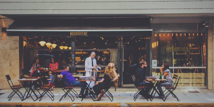A Restaurant General Manager having a conversation with customers seated outside of a restaurant.