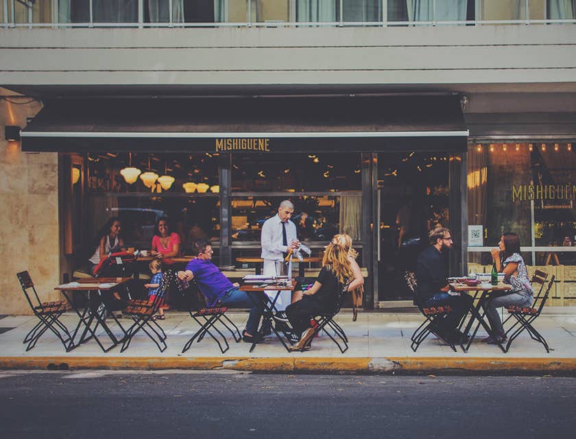 A Restaurant General Manager having a conversation with customers seated outside of a restaurant.
