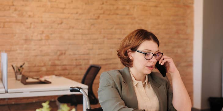 female retail banker sitting on her desk while using her phone and typing on her laptop