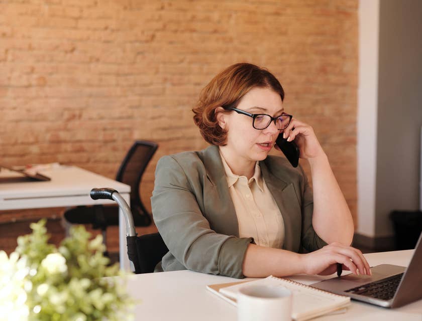 female retail banker sitting on her desk while using her phone and typing on her laptop