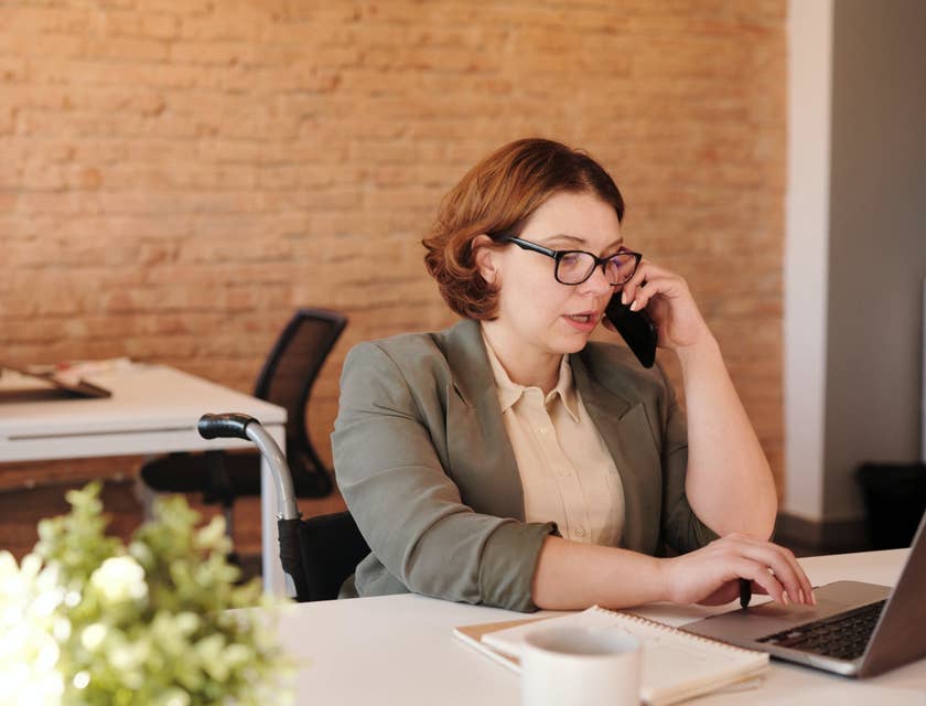female Retail Banker sitting on her desk while using her phone and typing on her laptop