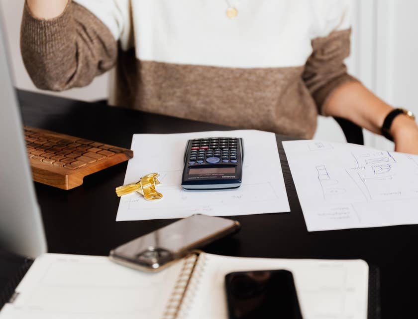Revenue cycle analyst calculates revenues using a calculator to prepare for a payroll report