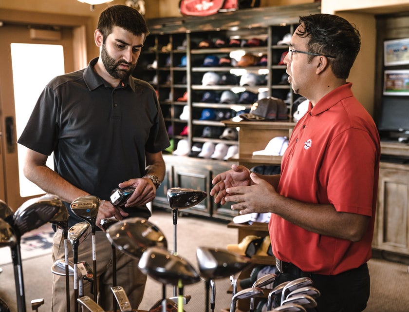 A sales representative selling golf clubs to a customer.
