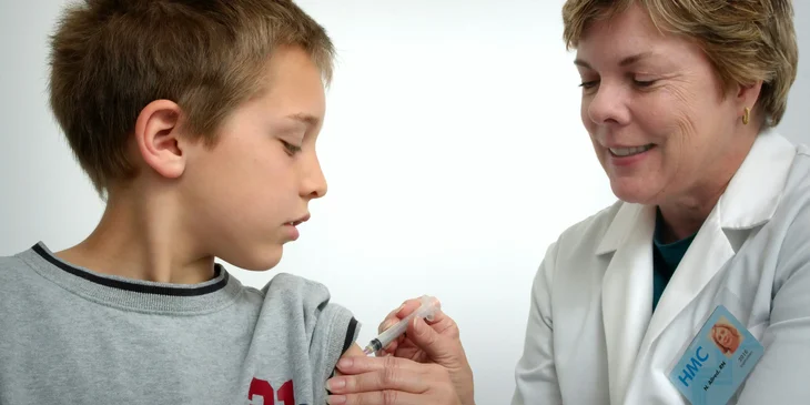 A school nurse gives a vaccine shot to a student in a school clinic.