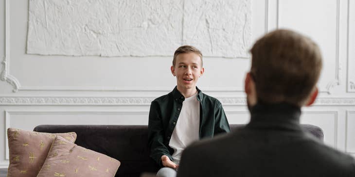 School social worker having a conversation with a male student sitting on the couch